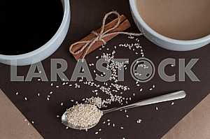 Black coffee and coffee with milk in white cups. Cinnamon and sesame.