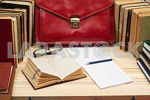 On a wooden table books, documents, calculator, red briefcase.