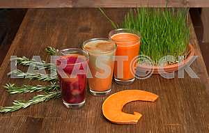 Various freshly squeezed vegetable juices with the hunk of pumpkin and germinating wheat on a wooden table.