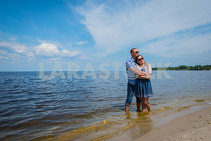 A loving couple standing in the river, embracing each other, blue sky on the background, sunny day, wide angle, long white clouds