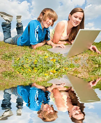 Two Smiling teenagers with laptop resting on meadow.