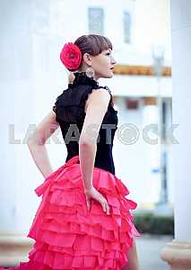 Woman Dancing carmen in saturated pink long curly skirt, with tied hair, and the flower in hair, in black blouse, among the column, portrait,