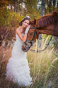 Brown-haired woman standing leaning to the horse, in wedding dress mermaid silhouette, among the spikelet, autumn, forest on the background
