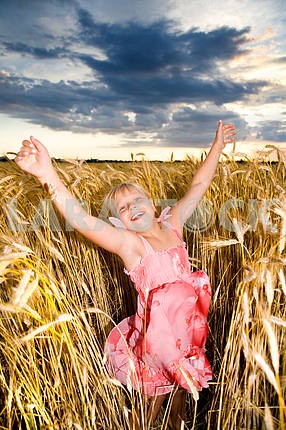 Little girl jumps in a wheat field. Against backdrop of cloudy s