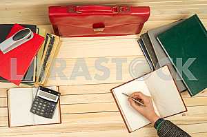 On a wooden table books, documents, calculator, red briefcase.