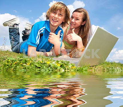 Два улыбается подростков с ноутбуком отдыхает на лугу . Отраженный я