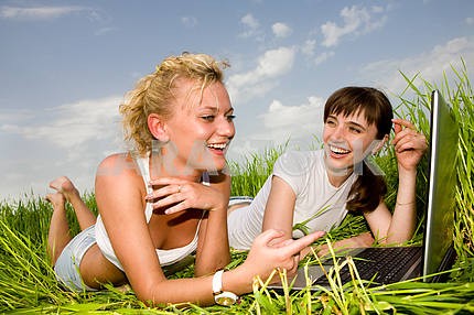 Two beautiful girls in white clothes are laughing near laptop co
