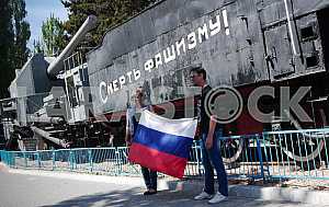 Люди позируют с российским флагом на фоне артиллерийского поезда "Железняков" в Севастополе.
