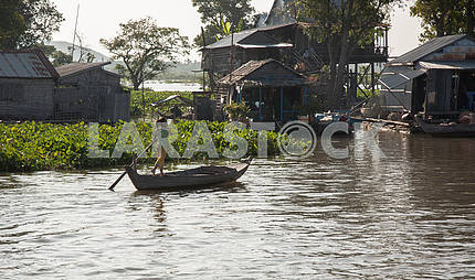 Little girl actively rowing oar, standing in a boat, Lake Tonle Sap
