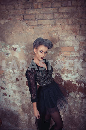 Woman dressed like a vampire - for halloween party, standing near the old brick wall . Short black tulle-skirt on a vampire-girl. looking angry like a devil. looking at you cunningly