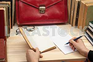 On a wooden table books, documents, calculator, red briefcase.