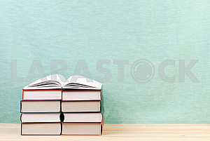 Открытая книга, стопка книг в твердом переплете на деревянном столе. Обратно в школу. Копирование пространства