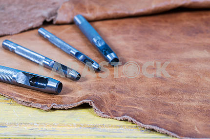 Leather craft tools on a wooden background. Leather craftmans work desk . Piece of hide and working handmade tools on a work table