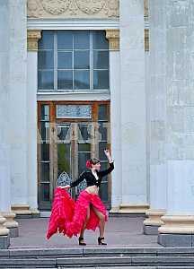 Woman Dancing carmen in saturated pink long curly skirt, with tied hair, and the flower in hair, in black blouse, among the column, showing her legs