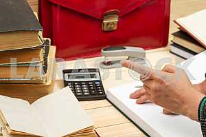On a wooden table books, documents, calculator, red briefcase.