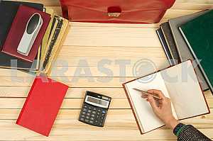 On a wooden table books, documents, calculator, red briefcase.