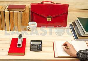 On a wooden table books, documents, calculator, red briefcase.