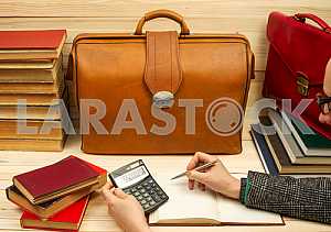 On a wooden table books, documents, calculator, red briefcase.