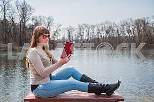 Young woman reading the book outdoor in sunglasses, daily lifestyle, river on the background, spring, sunny day