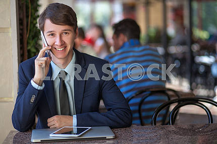 One relaxed young handsome professional businessman working with his laptop, phone and tablet in a noisy cafe. speak with phone.