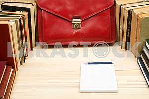 On a wooden table books, documents, calculator, red briefcase.