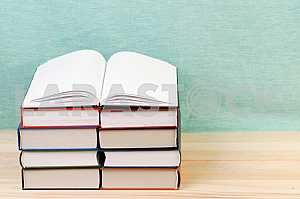 Открытая книга, стопка книг в твердом переплете на деревянном столе. Обратно в школу. Копирование пространства