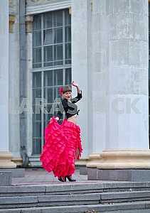 Woman Dancing carmen in saturated pink long curly skirt, with tied hair, and the flower in hair, in black blouse, among the column,