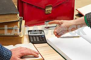 On a wooden table books, documents, calculator, red briefcase.