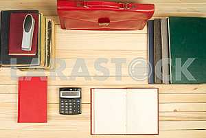 On a wooden table books, documents, calculator, red briefcase.