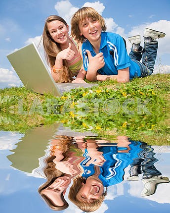Два улыбается подростков с ноутбуком отдыхает на лугу . Отраженный я
