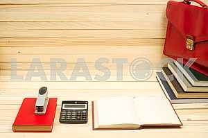 On a wooden table books, documents, calculator, red briefcase.