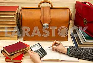 On a wooden table books, documents, calculator, red briefcase.