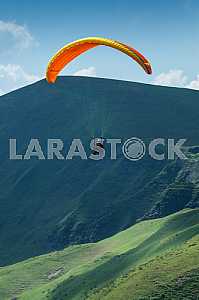 Paraglider flying over mountains on a summer day