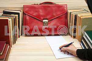 On a wooden table books, documents, calculator, red briefcase.