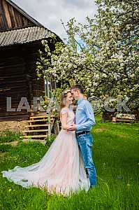 Couple in love looking at each other, almoust kissing, wooden old-time looking house on the background, flowering tree, green grass.