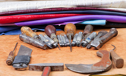 Инструменты для кожанного ремесла на деревянном фоне. Рабочий стол мастера по коже. Кусок шкуры и рабочие инструменты ручной работы на рабочем столе