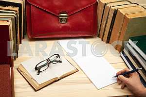 On a wooden table books, documents, calculator, red briefcase.