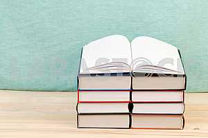 Открытая книга, стопка книг в твердом переплете на деревянном столе. Обратно в школу. Копирование пространства