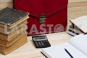 On a wooden table books, documents, calculator, red briefcase.