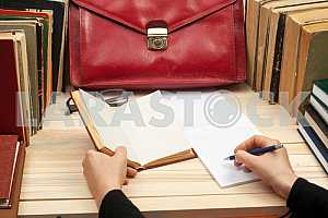 On a wooden table books, documents, calculator, red briefcase.