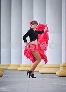 Woman Dancing carmen in saturated pink long curly skirt, with tied hair, and the flower in hair, in black blouse, among the column, showing her legs