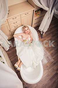 Blonde bride in wedding dress lying in bath, eyes up,