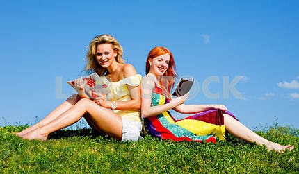 Two beautiful girls with notebook outdoors. Sitting on the green