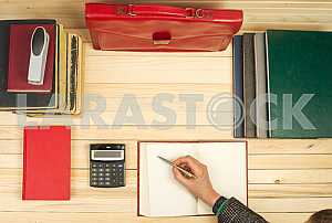 On a wooden table books, documents, calculator, red briefcase.