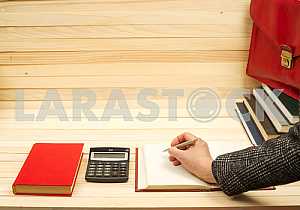 On a wooden table books, documents, calculator, red briefcase.