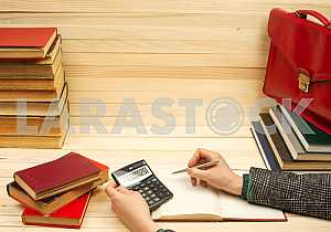 On a wooden table books, documents, calculator, red briefcase.