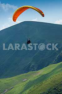 Paraglider flying over mountains on a summer day