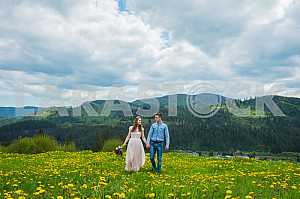 Wedding in mountains, a couple in love, mountains background, standing surrounded dandelions, among the lawn with the green grass, rustic style, girl in long tulle dress, romantic landscape, walking