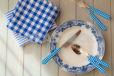 Empty plate, silverware and towel over wooden table background. View from above, blue colors