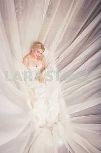 Blonde Bride in wedding dress lying in the bath with bouquet among the veil